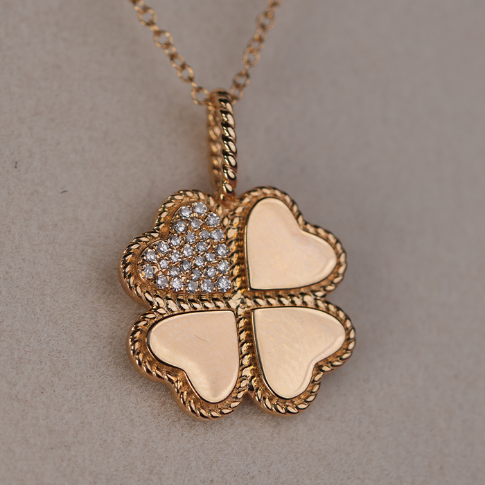 A gold pendant featuring four hearts, one of which is adorned with diamonds, on a gold chain against a neutral background.