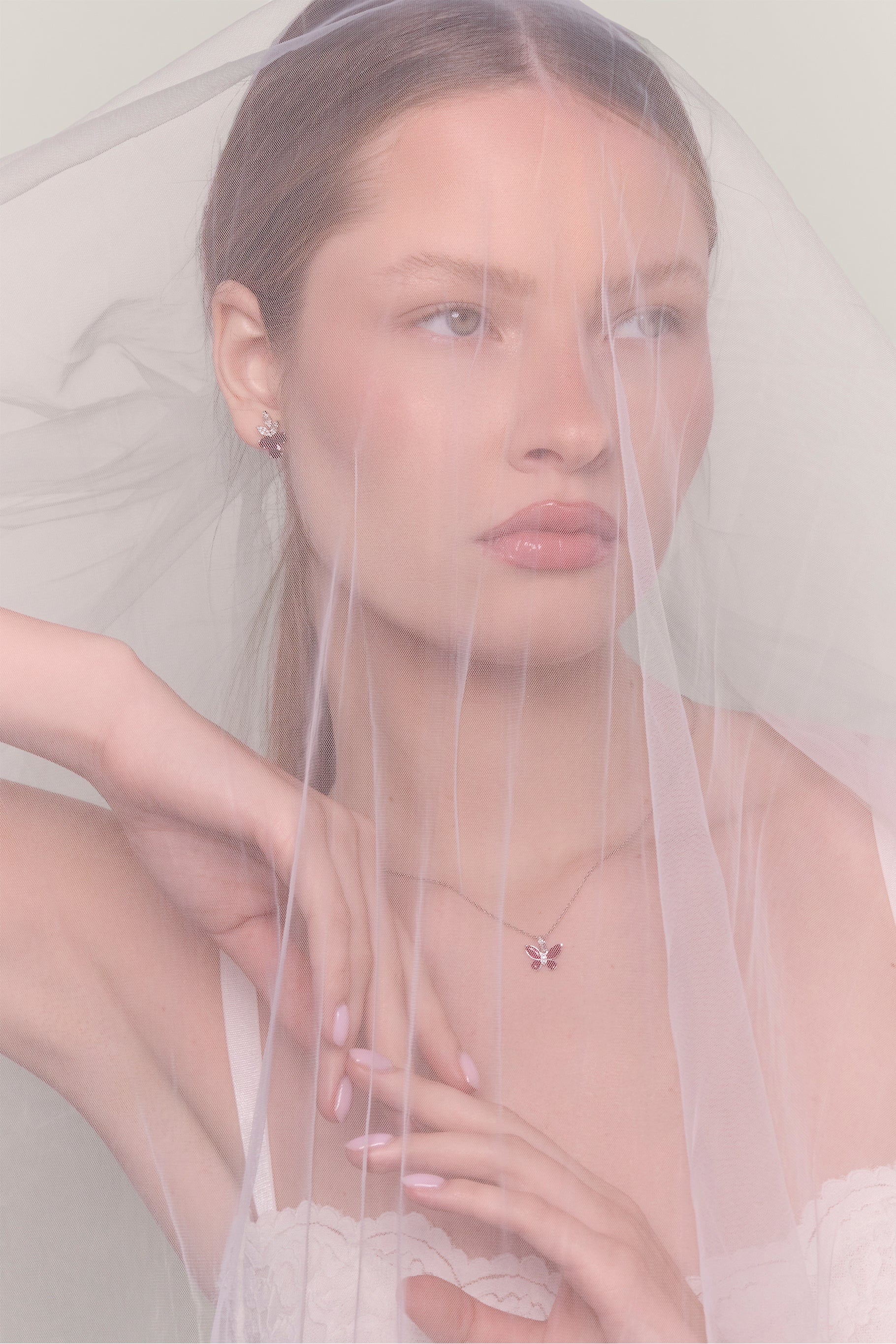 Head and shoulders side profile portrait under veil. Model wears the ruby butterfly pendant and diamond earrings.