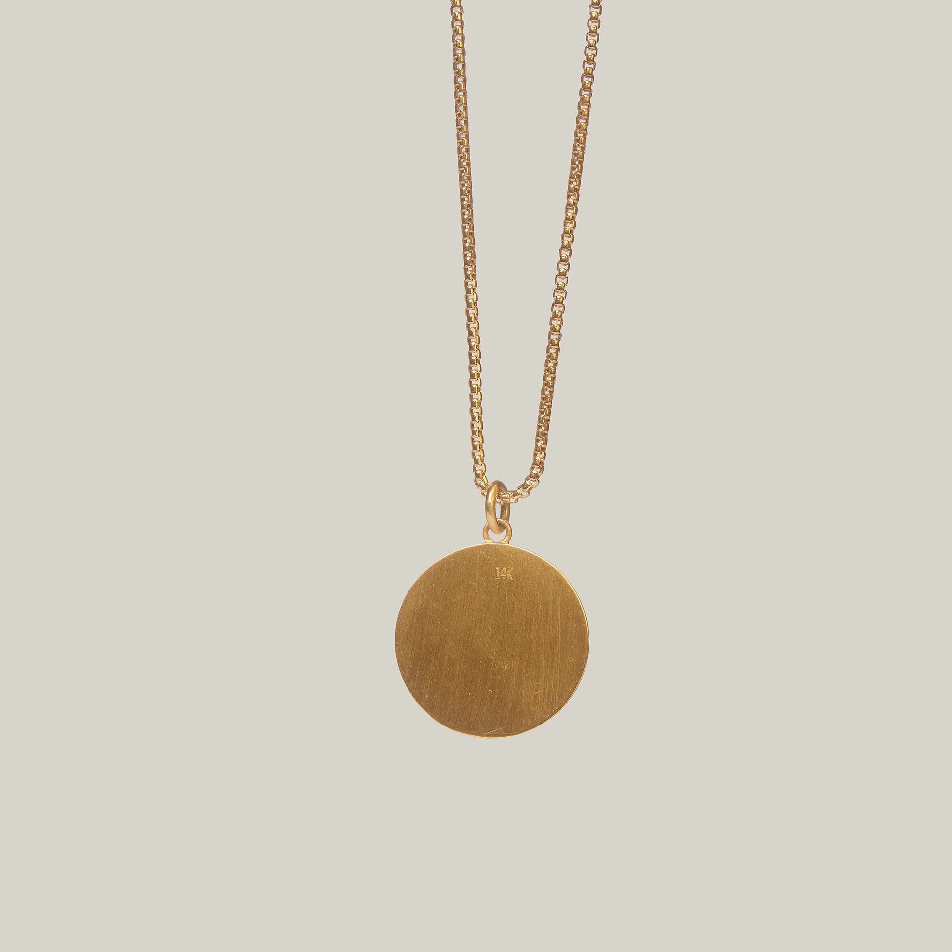 Close up rear view of a necklace with a circular pendant featuring sun and moon designs on a light gray background