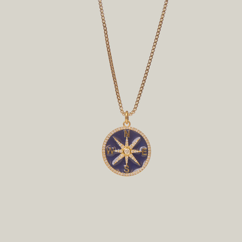 Close up front facing view of a compass pendant on a light gray background