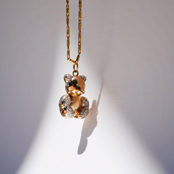 A 14k gold bear pendant with pave-set diamond sections, suspended from a gold chain against a white background.