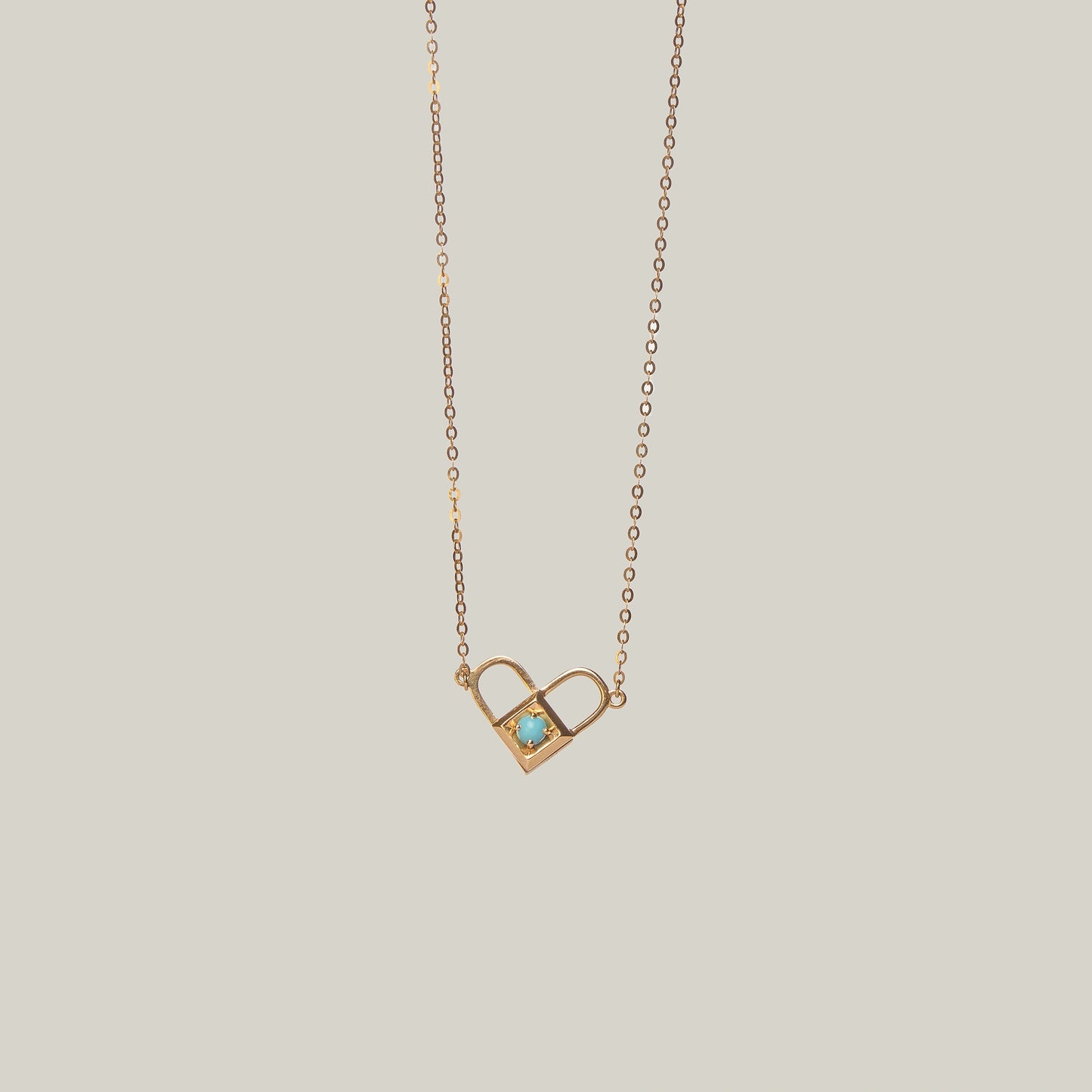 Close-up rear-facing view of an opened gold and turquoise padlock necklace with heart shape on a light gray background