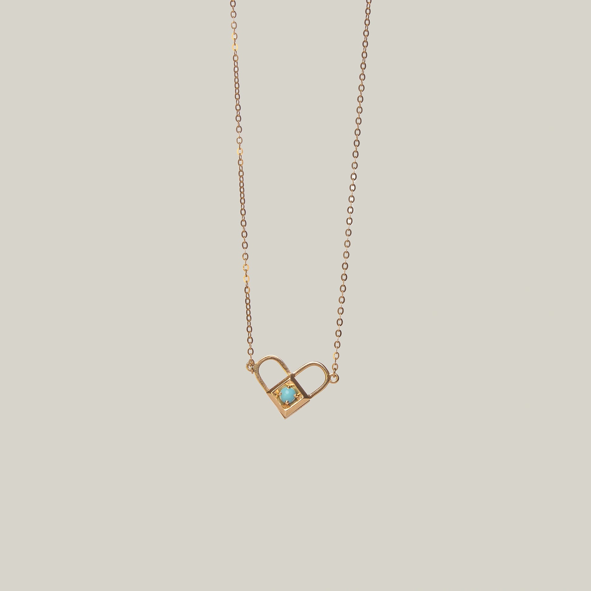 Close-up rear-facing view of an opened gold and turquoise padlock necklace with heart shape on a light gray background