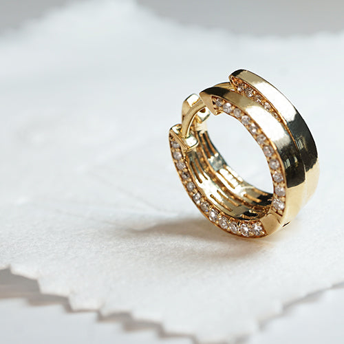 A pair of 14k yellow gold hoop earrings with white diamond pave, displayed on a white textured surface.