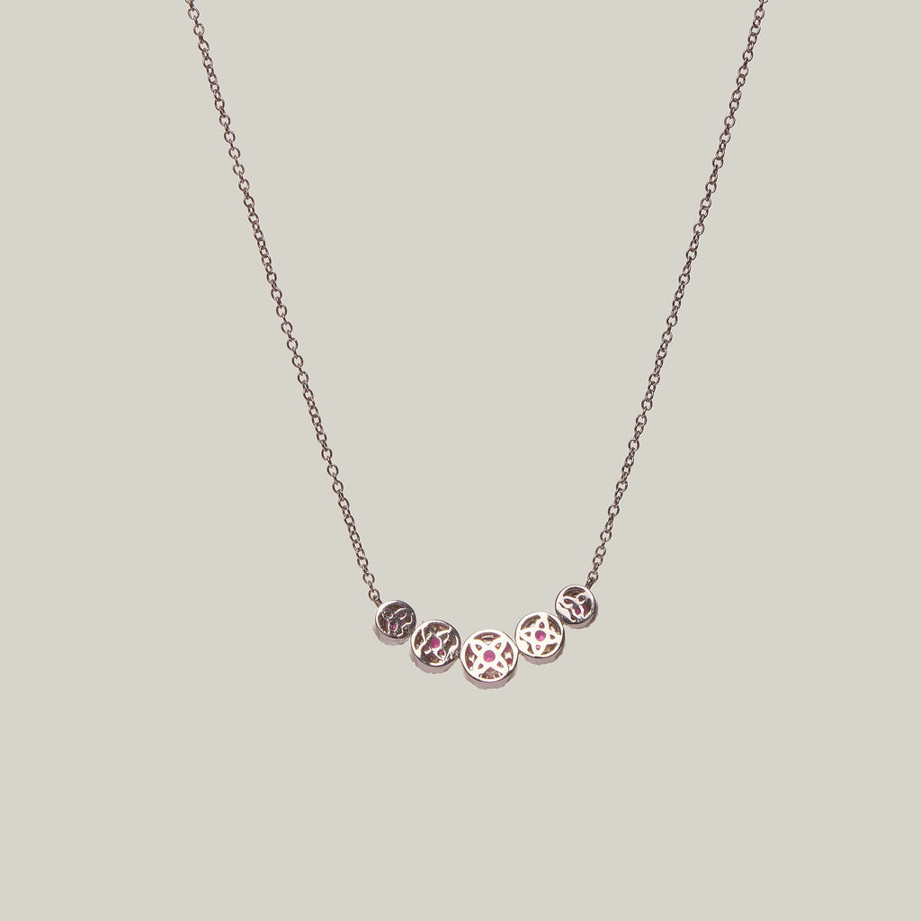 Rear view of a gold necklace with rubies in a curved pattern on a light gray background