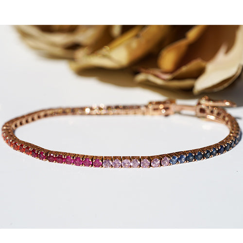 A multicolored sapphire bracelet with pink, blue, lilac and red gemstones on a white background with gold flowers