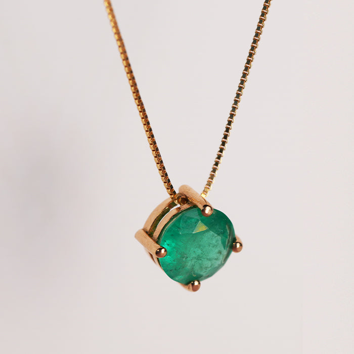 A sphrerical emerald necklace in a gold four-prong setting with a matching chain against a white background.