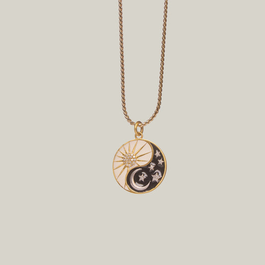 Close up front view of a necklace with a circular pendant featuring sun and moon designs on a light gray background