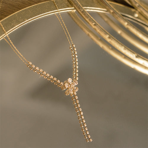A delicate diamond lariat necklace in 14k gold, featuring a flower shaped centerpiece, positioned on a reflective mirror background.