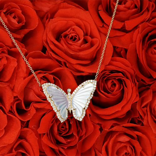 A yellow gold necklace with a butterfly pendant featuring hand set diamonds, displayed against a red rose background.