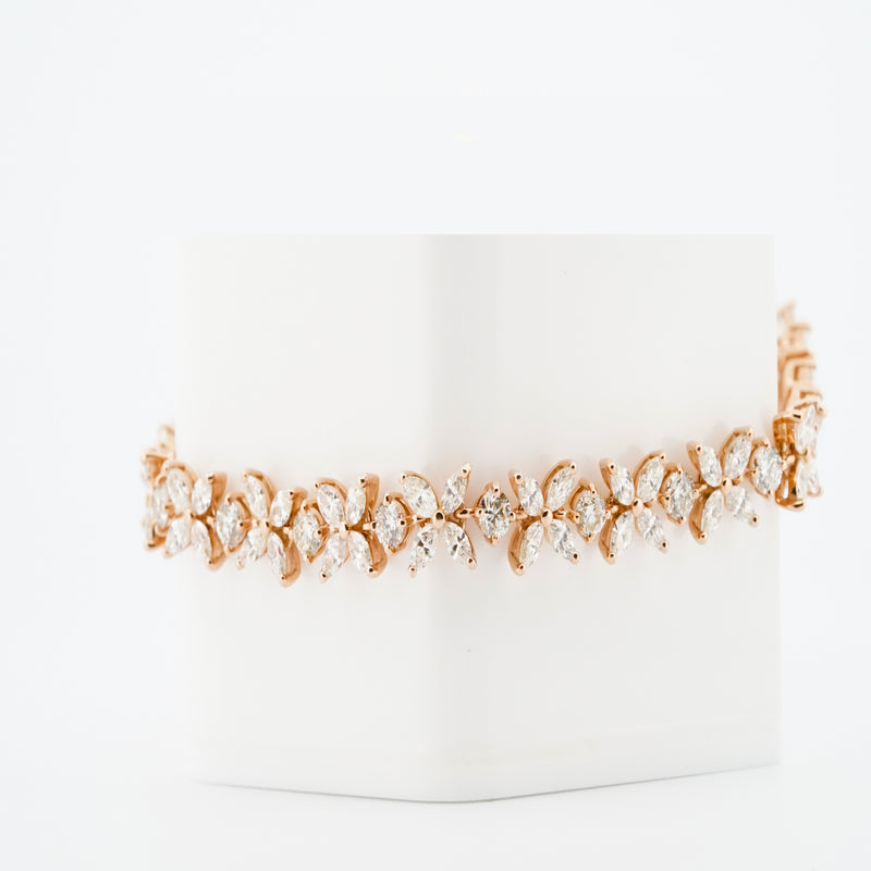 A gold bracelet featuring diamond flowers in a repeating pattern, shown on a white block against a matching background.