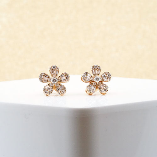 Close up view of gold diamond earrings with a flower design, shown on a white block against a cream background.