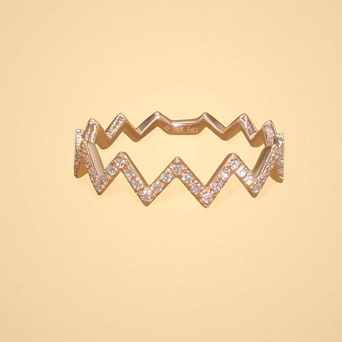 A gold ring encrusted with diamonds in a zig zag design, displayed against a cream background.