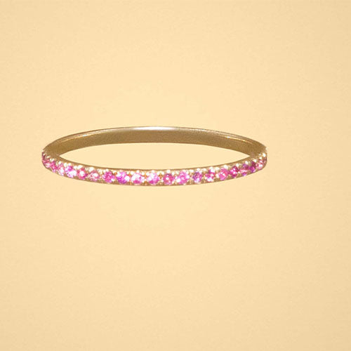 A yellow gold ring with pink sapphires displayed on a dark cream background.