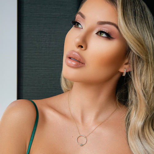 Model wears a pair of 14k gold diamond earrings with a snake necklace against a neutral background.